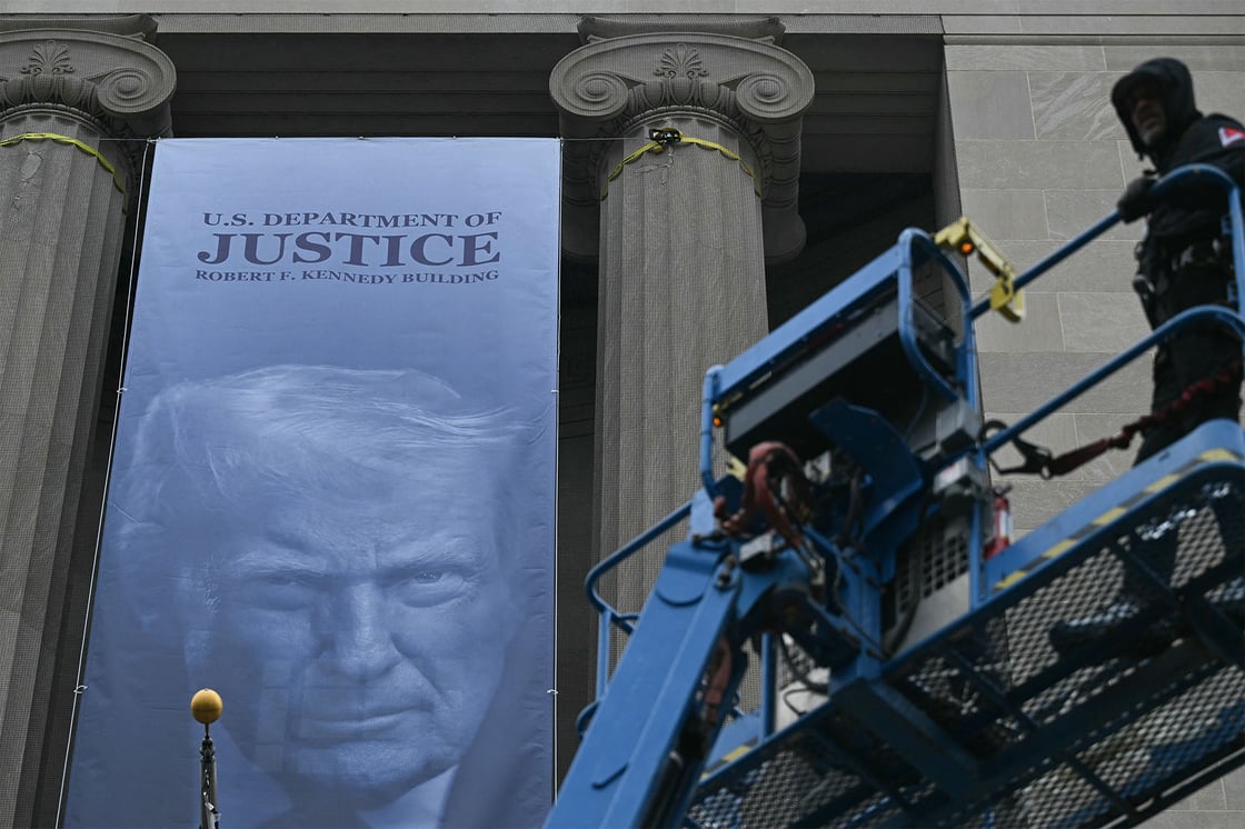 Workers check their installation of a new banner featuring an image of U.S. President Donald Trump on the facade of the U.S. Department of Justice headquarters building in Washington, D.C., in February 2026. (Getty/Brendan Smialowski/AFP)