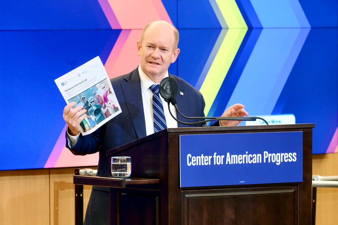 Sen. Coons holding up a printed page from the new report at a podium.