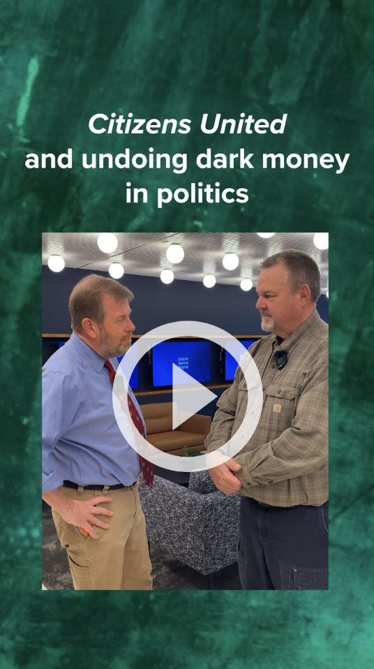 Two men - Tom Moore and Sen. Jon Tester - speaking to one another in a conference room.